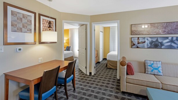 A hotel room with a dining area, a sofa, and a bed. There are framed pictures on the walls, a clock, and a thermostat. - MainStay Suites Mt. Laurel - Philadelphia (Mount Laurel)