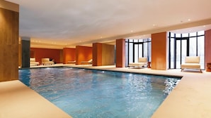 A modern indoor pool area with clear water, beige tiled flooring, and a row of beige chairs along the pool's edge. - Montebelo Viseu Congress Hotel & Spa (Viseu)