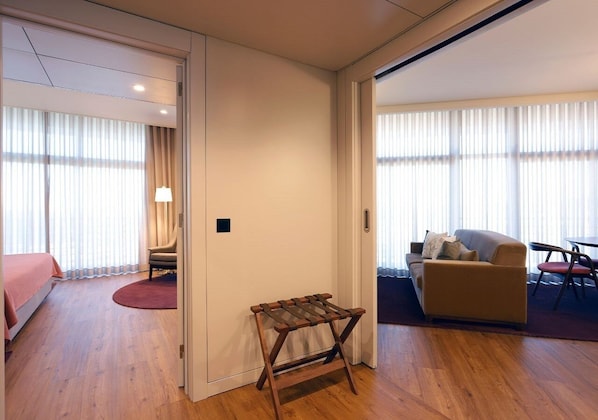 A hotel room with a bed, a chair, a small table, a sofa, and a dining table.