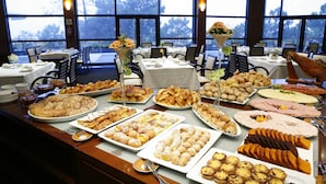 A buffet with various dishes and a view of trees through large windows. - Montebelo Viseu Congress Hotel & Spa (Viseu)