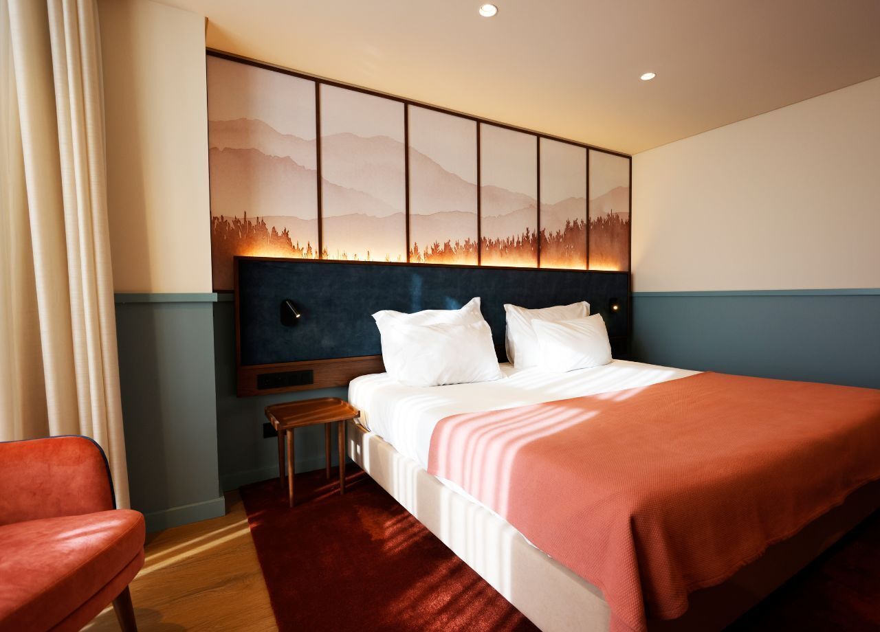 A hotel room with a bed, a nightstand, a chair, and a wall-mounted artwork.