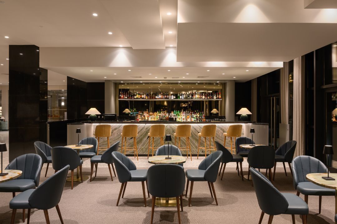 A bar area with a marble countertop, multiple bar stools, and a variety of bottles.