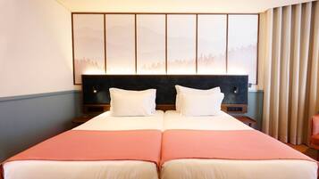 A double bed with two pillows, a headboard with a cityscape artwork, and a window with curtains.