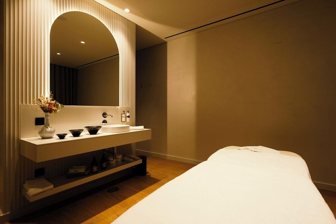 Quarto de hotel moderno com um espelho grande, uma toucador branca com pia e uma cama bem arrumada.