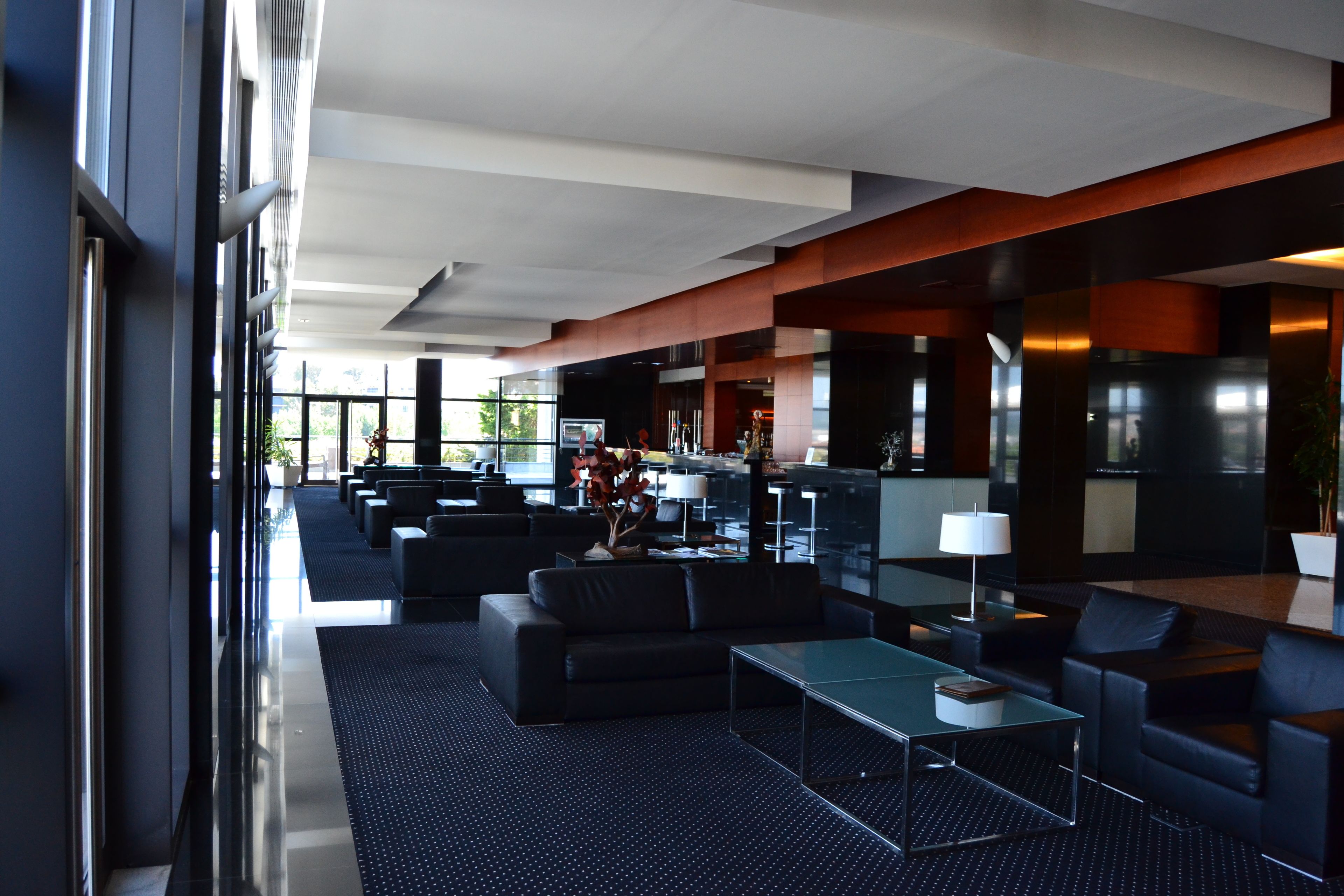 A modern hotel lobby with a spacious seating area, a bar, and large windows providing natural light.