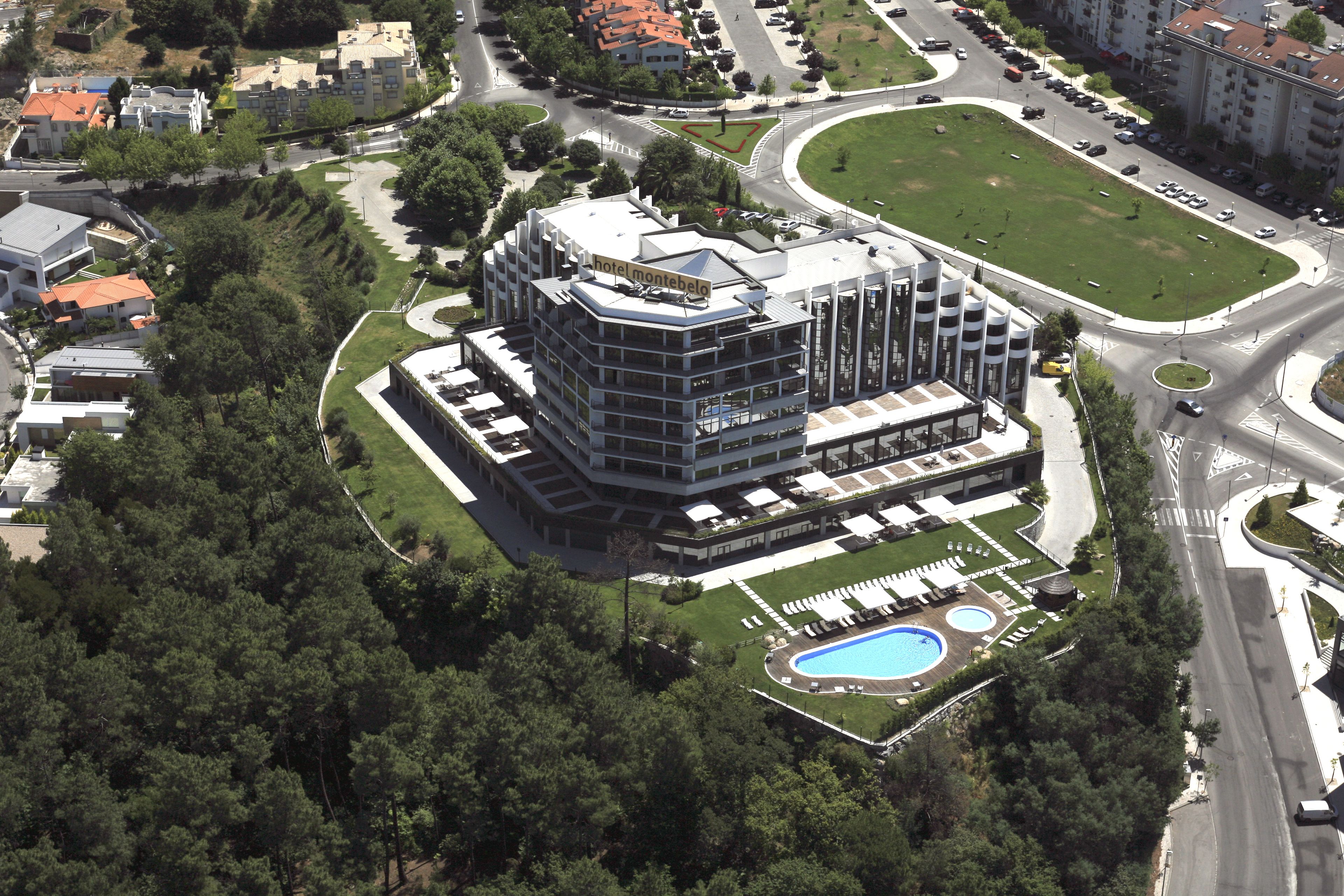 Ein modernes Hotel mit Pool auf dem Dach, umgeben von Grün und neben einer Straße.