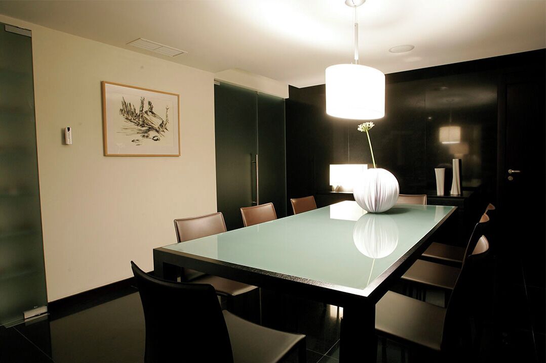 Un salón de conferencias con una mesa de vidrio, sillas, una obra de arte enmarcada y una lámpara colgante moderna.