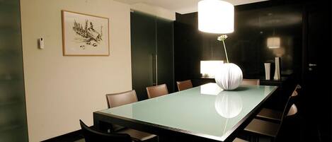 Un salón de conferencias con una mesa de vidrio, sillas, una obra de arte enmarcada y una lámpara colgante moderna.