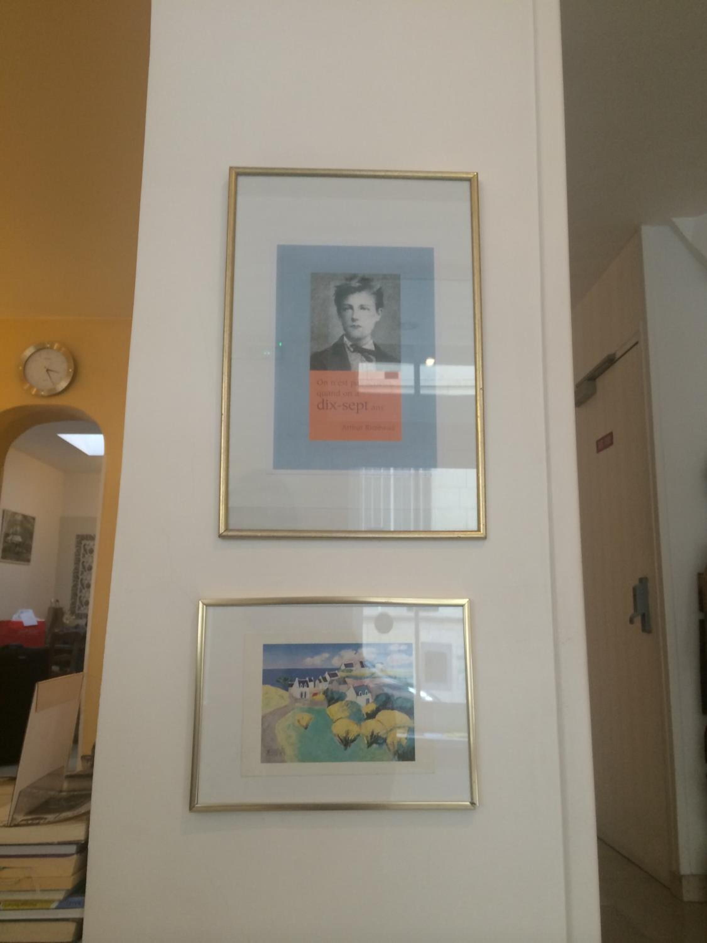 To billeder hænger på en væg, et med et portræt og det andet med et landskab.