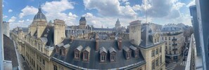 A cityscape with historic buildings, including a prominent dome and a large clock tower. - Hôtel Cluny Sorbonne (Paris)