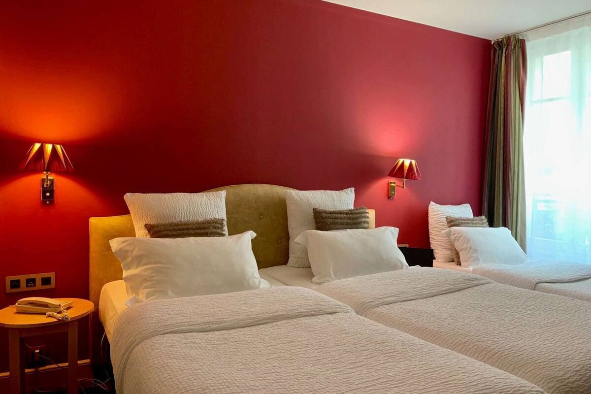 A hotel room with two beds, red walls, and two wall-mounted lamps.