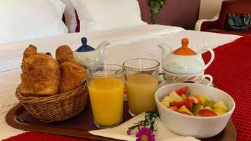 Ein Frühstückswagen mit Croissants, Orangensaft und einer Obstschale auf einem Bett.