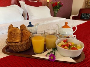 A breakfast tray with croissants, orange juice, and a fruit bowl on a bed. - Hotel Central Saint Germain (Paris)