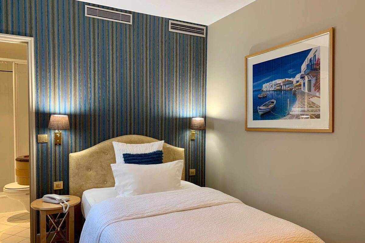 A hotel room with a large bed, two bedside lamps, a framed picture of a coastal scene, and a striped wall.