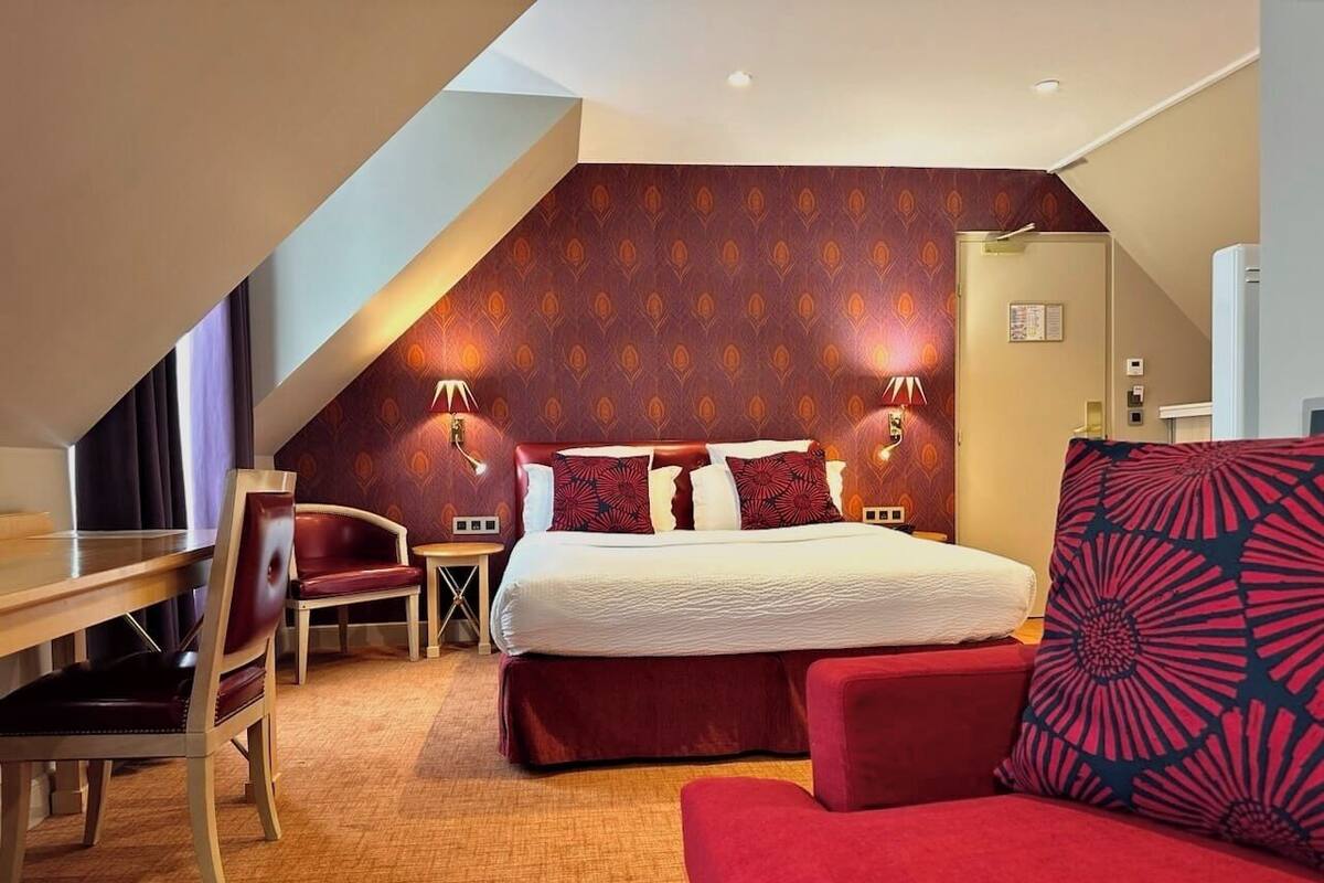 A hotel room with a bed, a desk, a chair, and a red sofa.