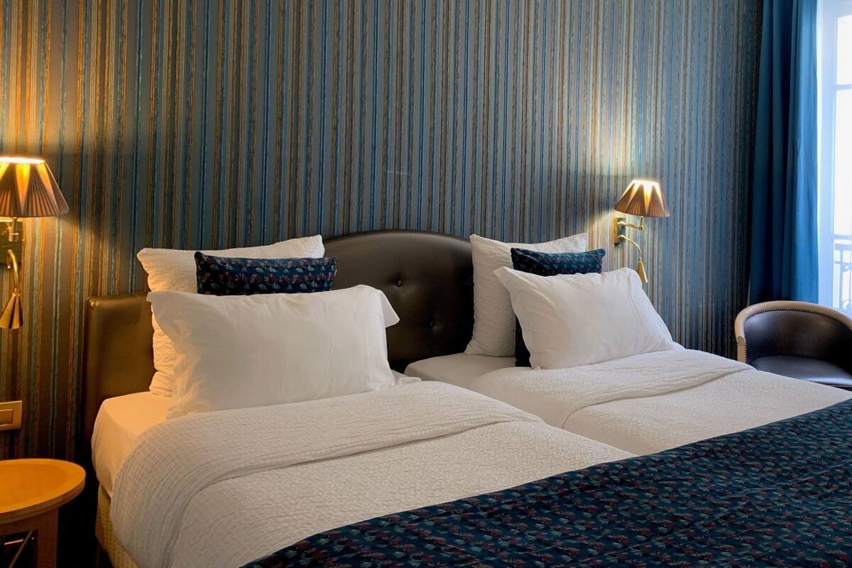 A hotel room with a large bed, two bedside lamps, a chair, and a view of the outdoors through a window.