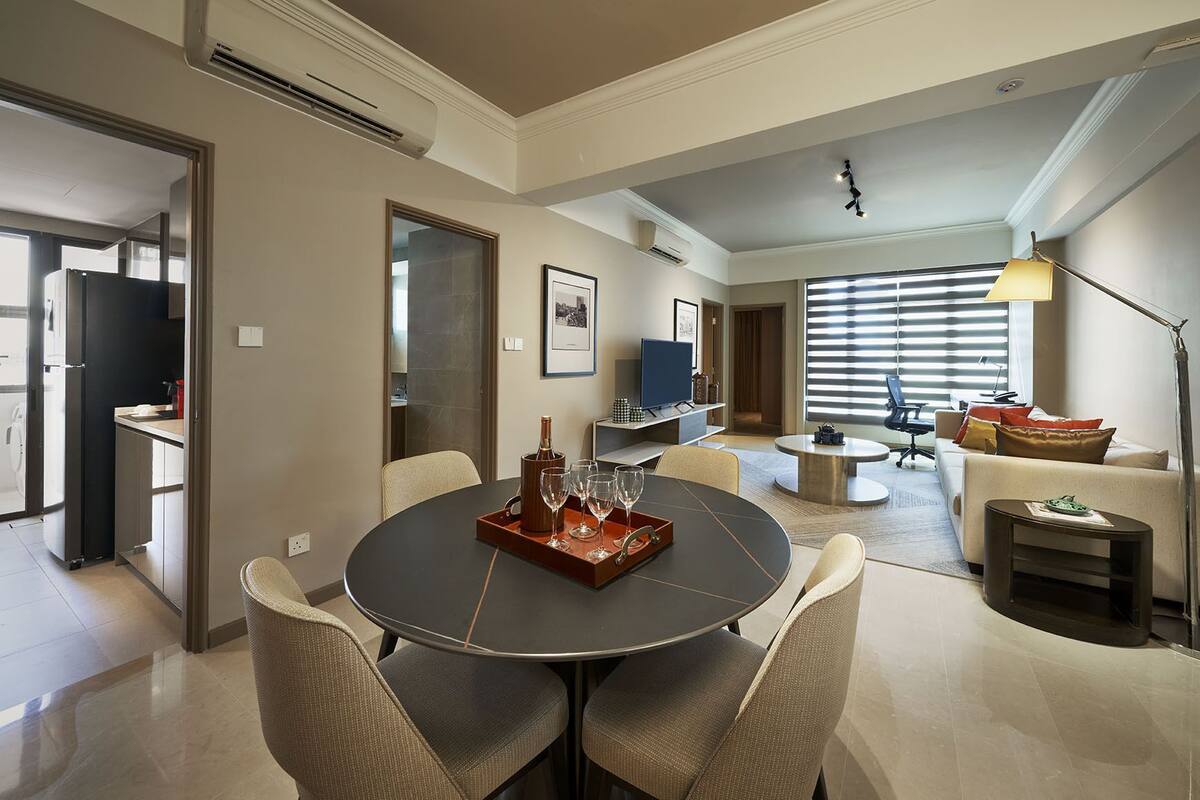 A modern living room with a round dining table, comfortable seating, a television, and a large window with blinds.