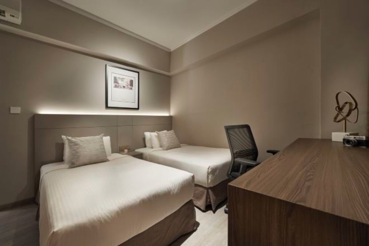 Quarto de hotel com duas camas, uma escrivaninha e uma cadeira.