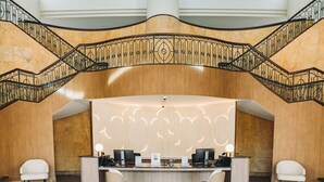 A reception desk with two chairs, a curved staircase with ornate railings, and a high ceiling with skylights. - Great World Residences (Singapore)