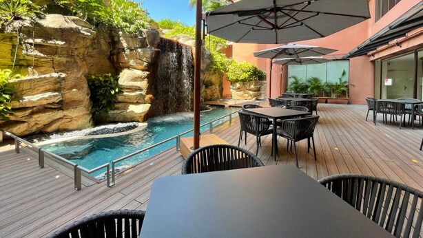 A rooftop pool area with a waterfall, surrounded by outdoor seating and a stone wall. - Great World Residences (Singapore)