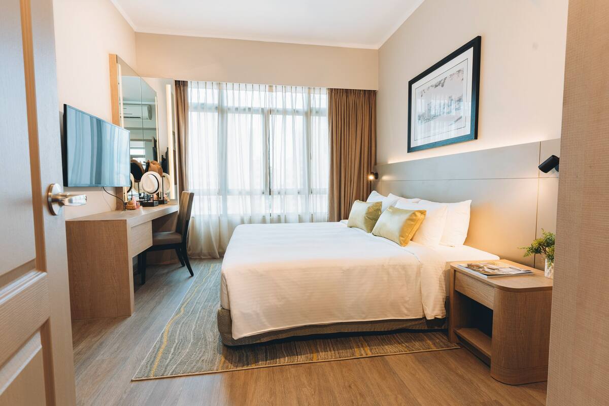 A hotel room with a large bed, a desk with a mirror, a television, and a framed picture on the wall.