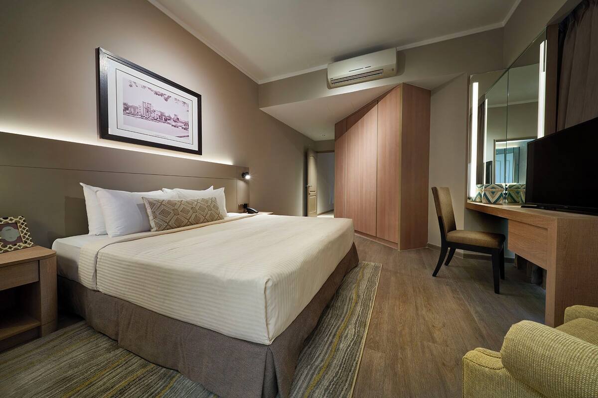A hotel room with a large bed, a desk with a TV, a chair, and a wardrobe.