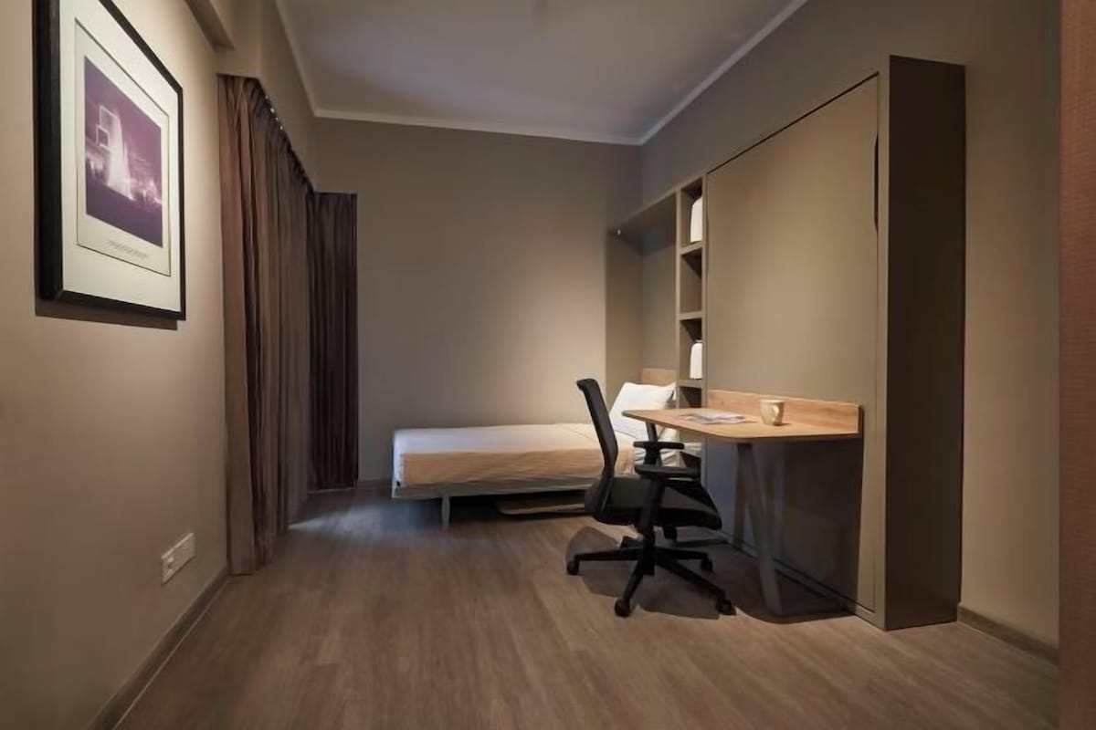 Una habitación de hotel compacta con una cama individual, un escritorio con silla y un armario.