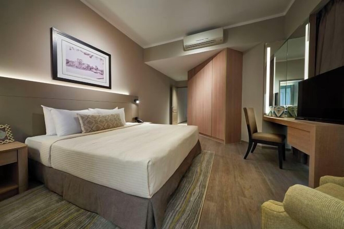 Een hotelkamer met een groot bed, een bureau met stoel, een televisie en een fotokader aan de muur.