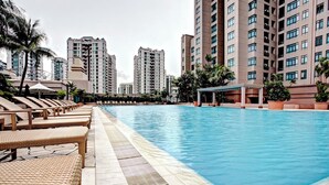 A swimming pool with lounge chairs and a covered seating area, surrounded by tall residential buildings. - Great World Residences (Singapore)