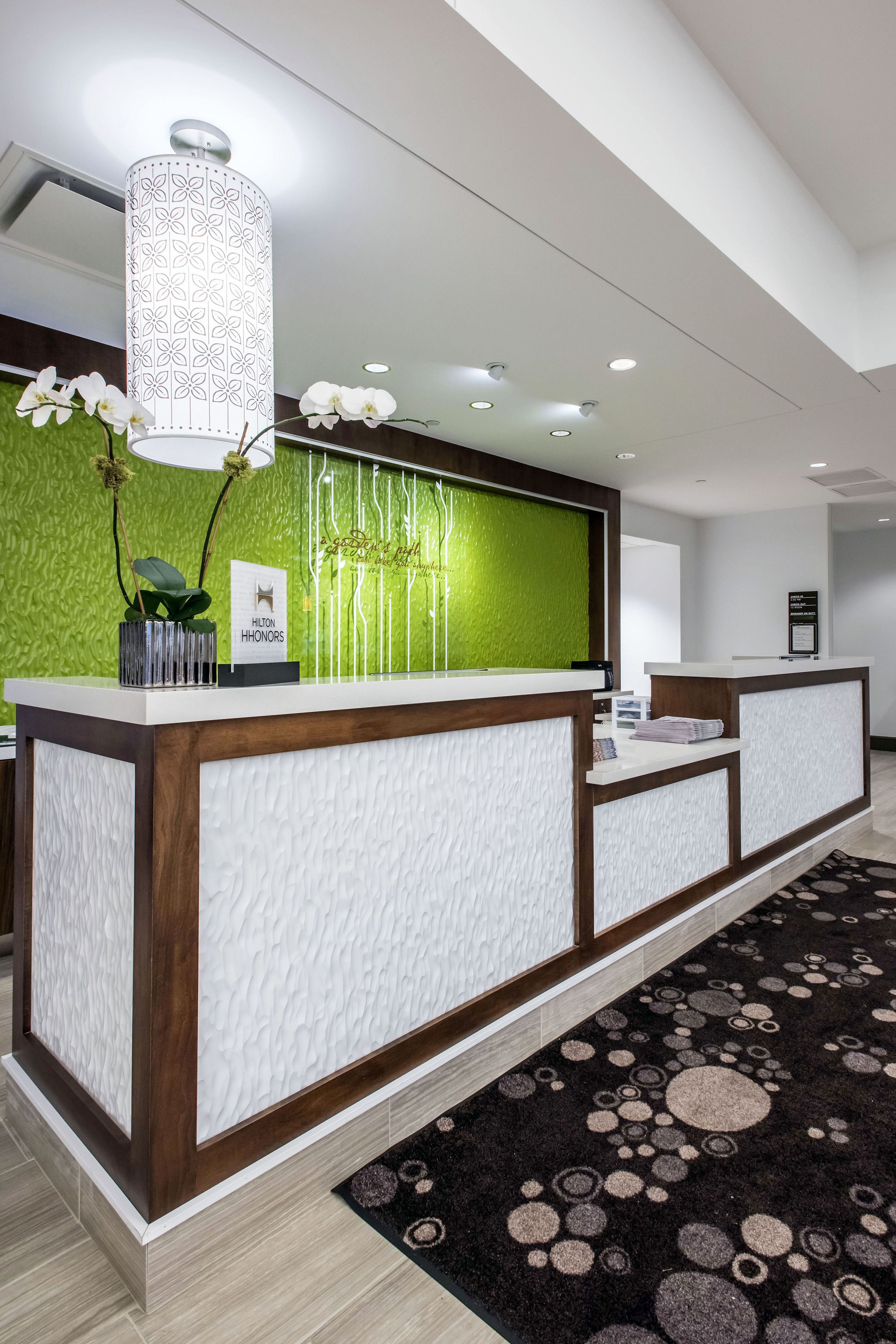 A hotel reception desk with a green wall, a white textured counter, and a hanging light fixture.