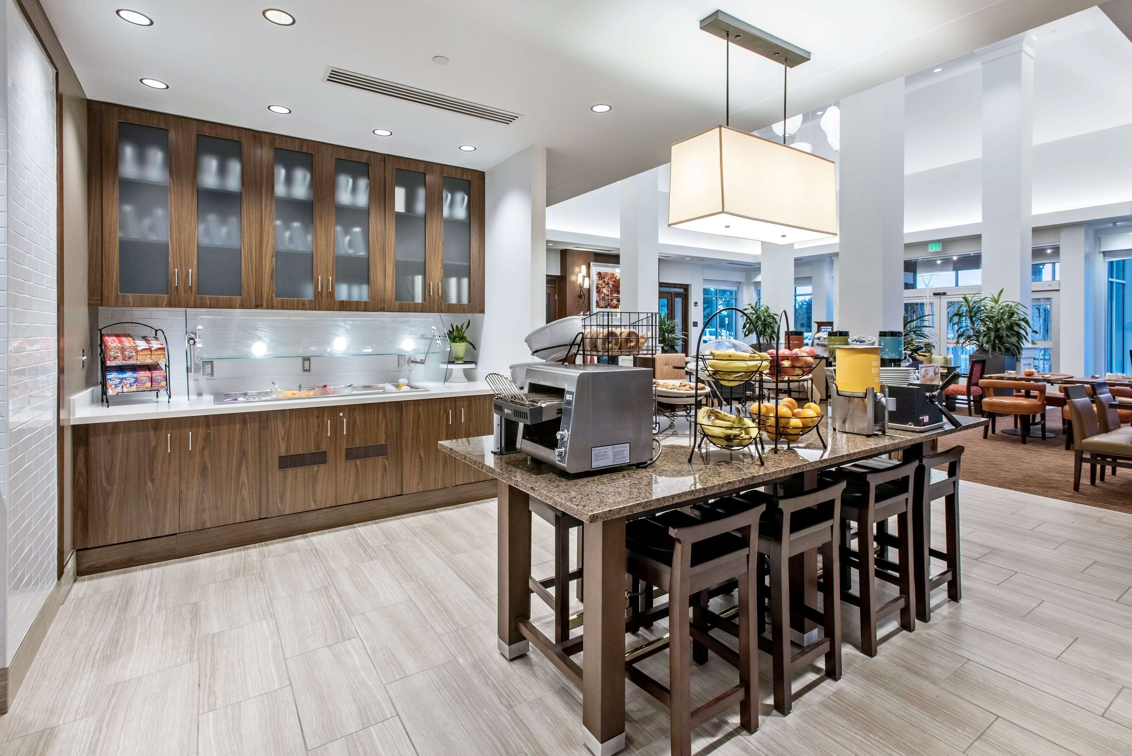 Une cuisine moderne avec des meubles en bois, un îlot central doté de tabourets de bar, une machine à café et un présentoir à fruits.