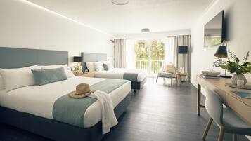 Habitación de hotel con dos camas, un escritorio, una silla, un televisor y un balcón con cortinas.