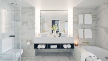 Ein modernes Badezimmer mit Duschkabine aus Glas, einem Doppelwaschtisch, einer Badewanne und Marmorwänden.