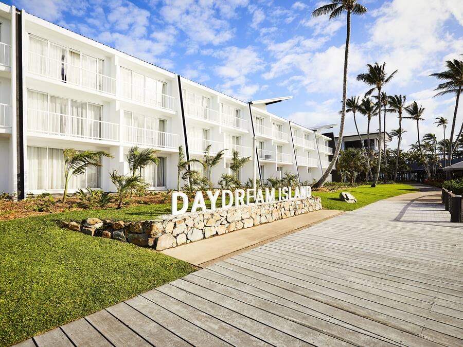 A hotel with a white facade, a stone pathway, and palm trees.