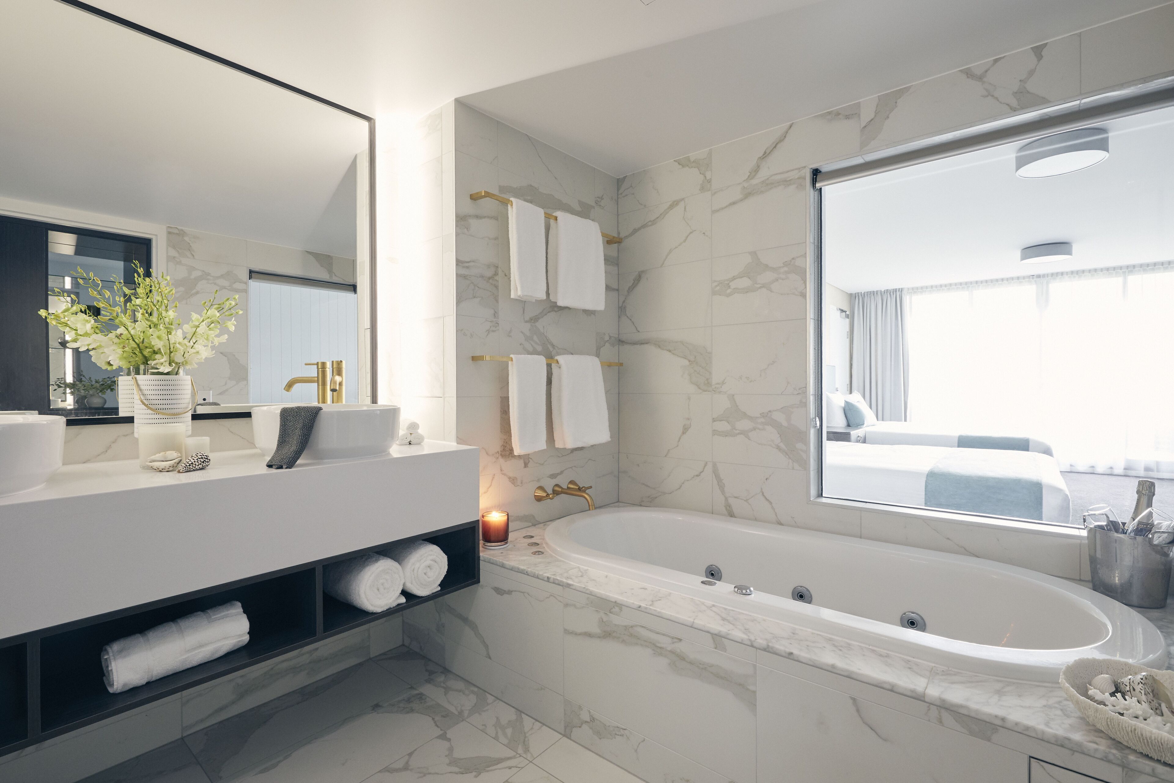 Un bagno moderno con parete in marmo, una vasca da bagno ampia, un mobile lavabo con specchio e una finestra che offre vista sulla stanza.