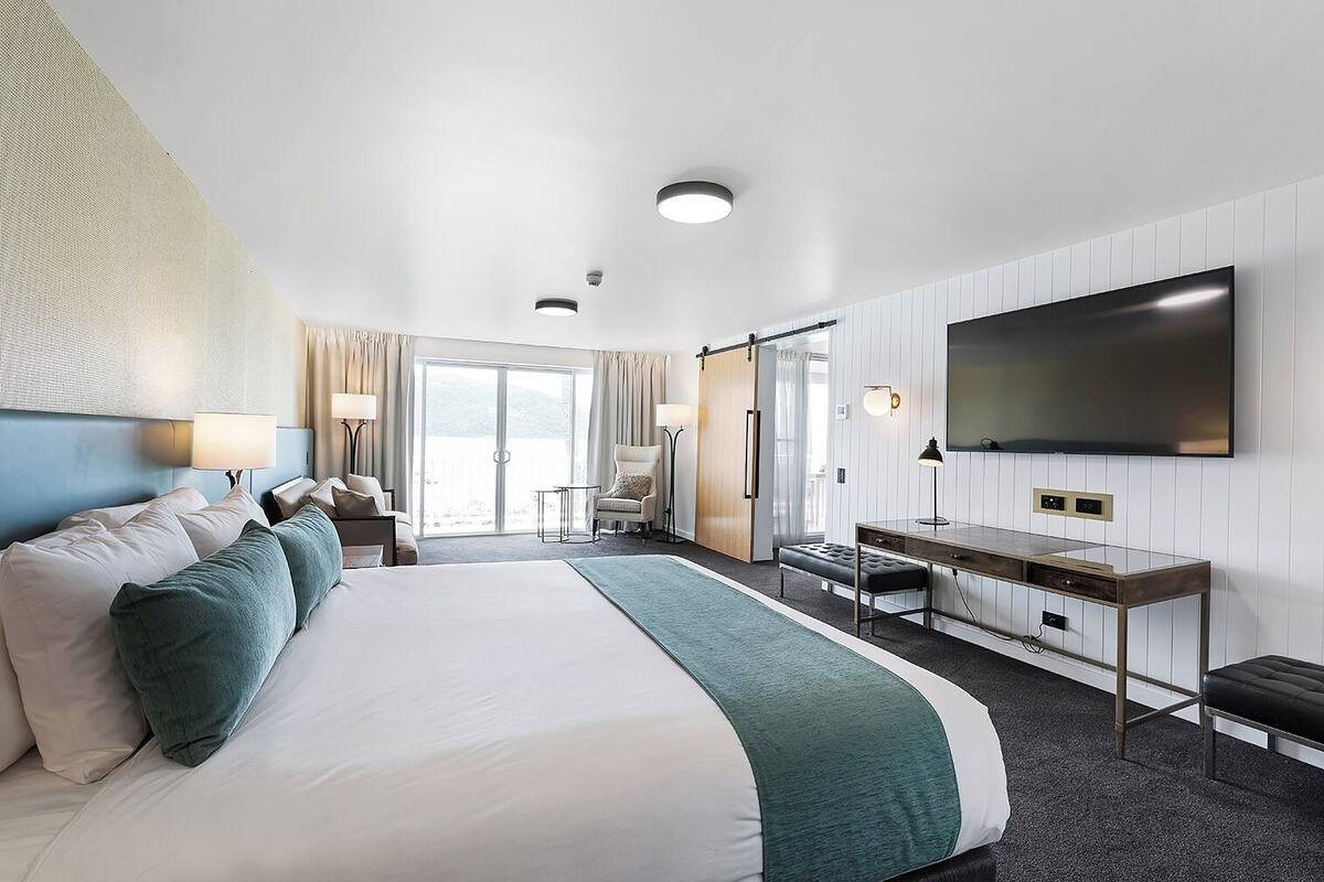 Habitación de hotel con una cama grande, un escritorio, un televisor de pantalla plana y una puerta corredera a un balcón.