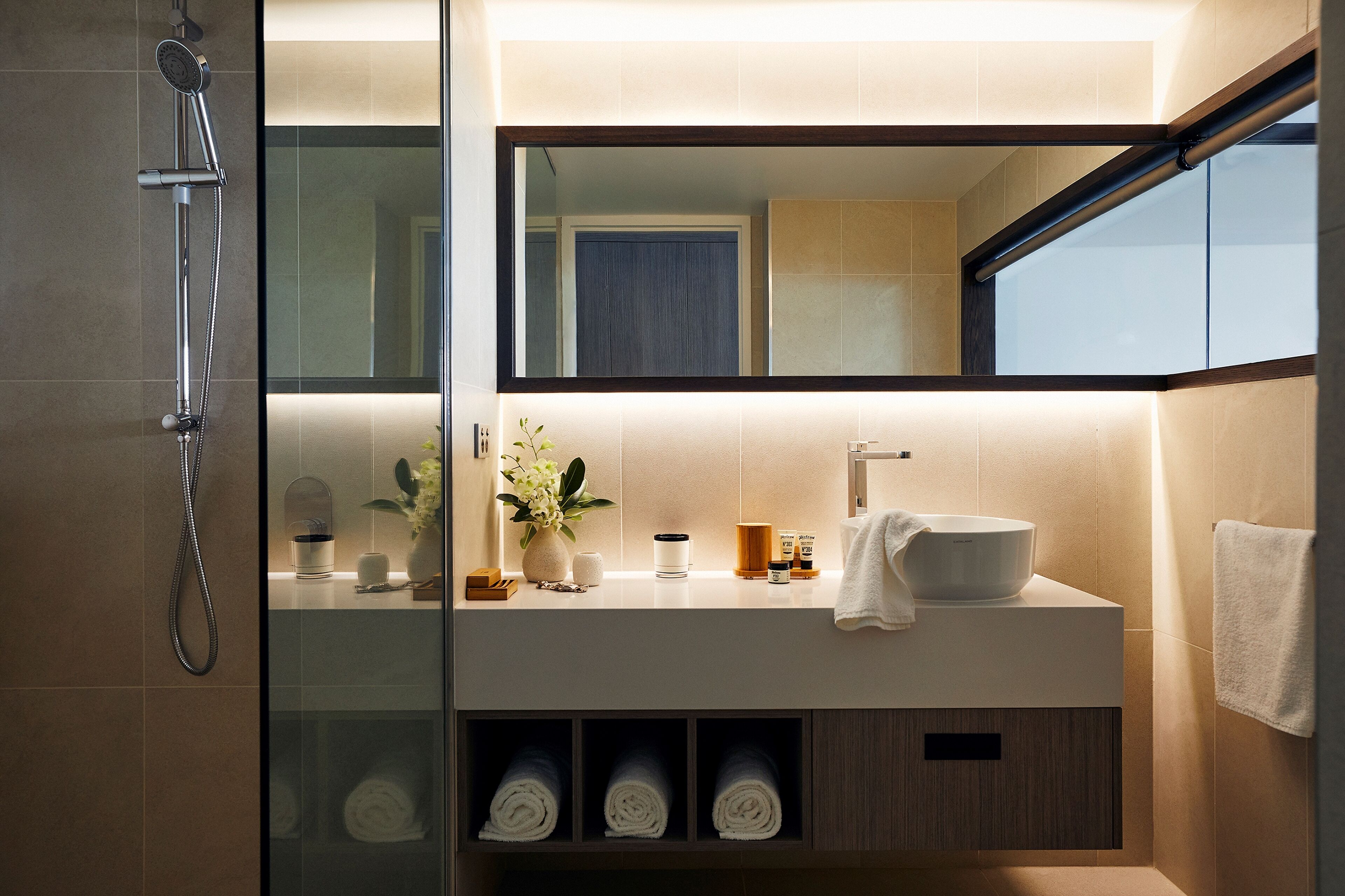 Un baño moderno con ducha envuelta en cristal, un espejo grande y un tocador con lavamanos y toallero.