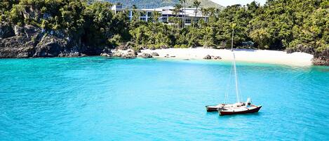 A boat on turquoise water with a beach and buildings in the background.