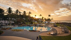 Un resort con una piscina grande, palmeras y vistas al océano al atardecer.