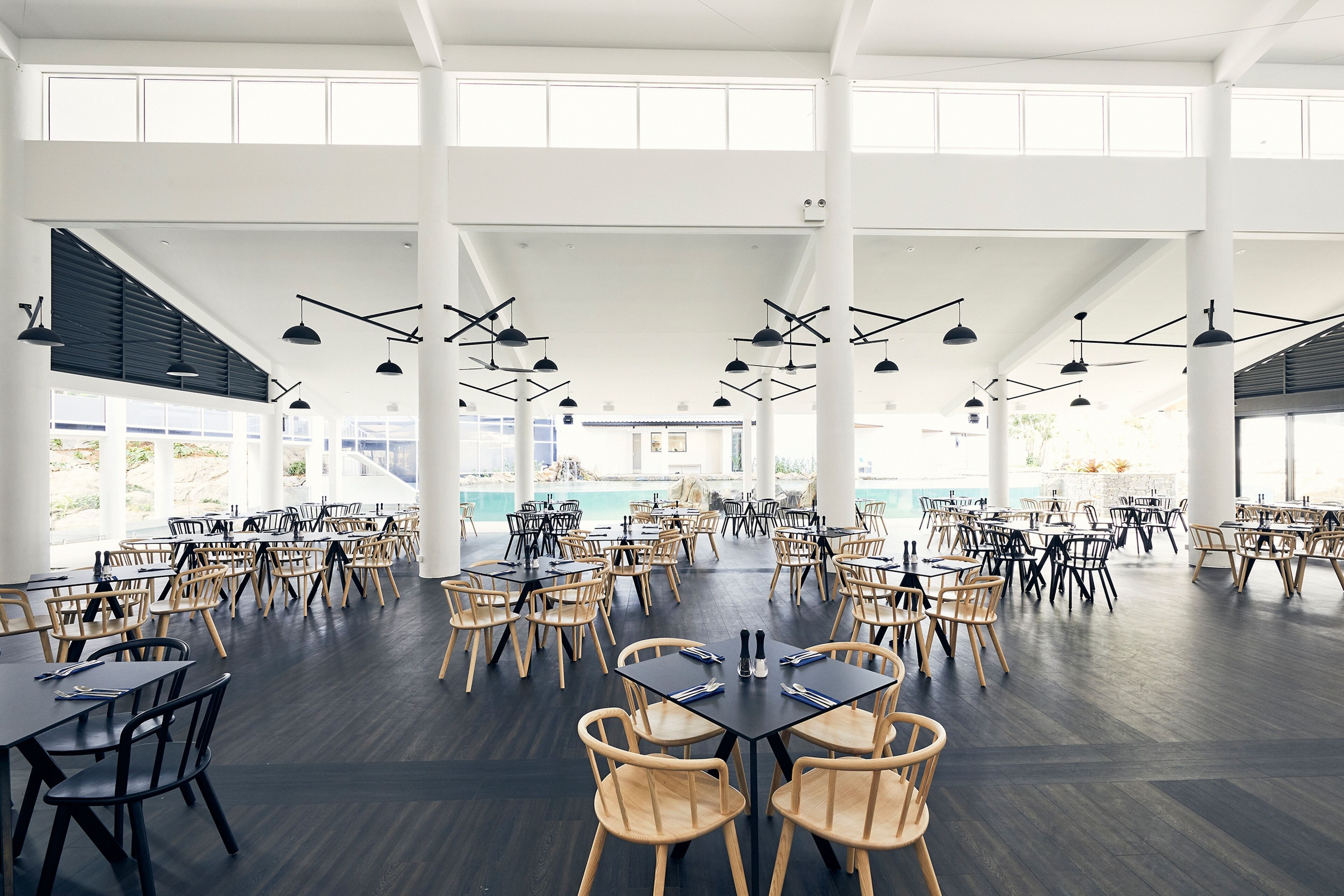 A spacious indoor dining area with multiple tables and chairs, large windows, and hanging pendant lights.