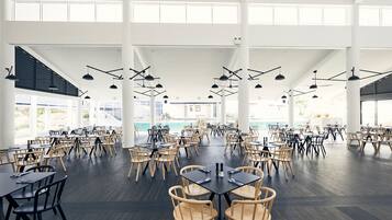 A spacious indoor dining area with multiple tables and chairs, large windows, and hanging pendant lights.