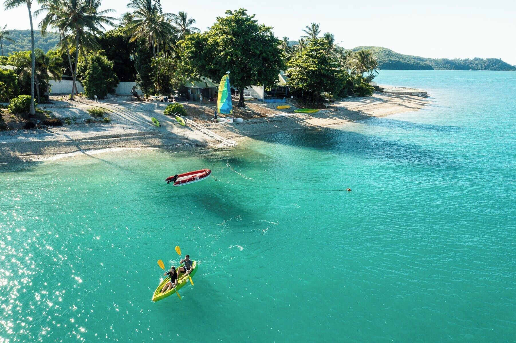 A beach with clear turquoise water, a kayak with two people, and a small boat anchored nearby.