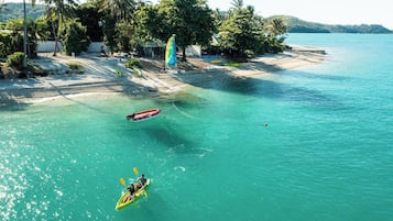 Una playa con agua turquesa cristalina, un kayak con dos personas y una pequeña embarcación anclada cerca.