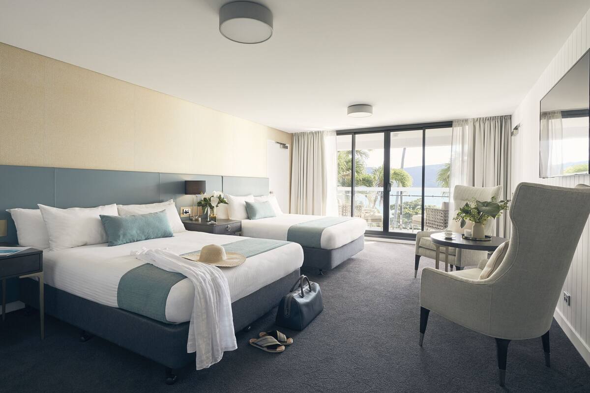 Habitación de hotel con una cama grande, dos mesitas de noche, una silla, una pequeña mesa y vistas al exterior.