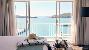 Habitación de hotel con un amplio ventanal corredero que da a un balcón con vistas a un lago y colinas distantes.