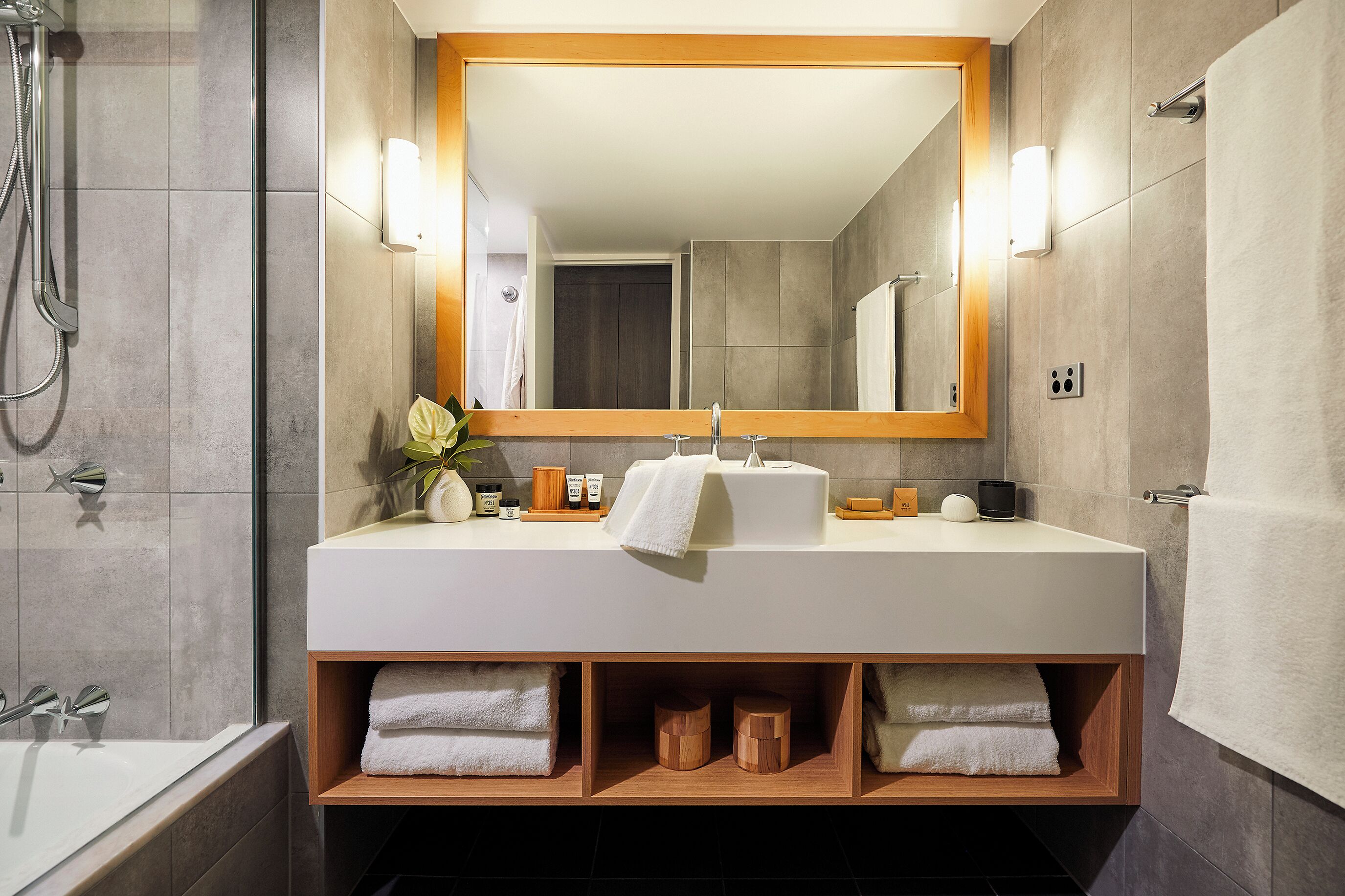 A modern bathroom with a large mirror, white sink, and built-in shelves for towels.