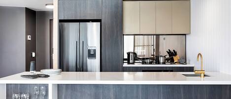 A modern kitchen with a stainless steel refrigerator, a coffee maker, and a gold faucet.