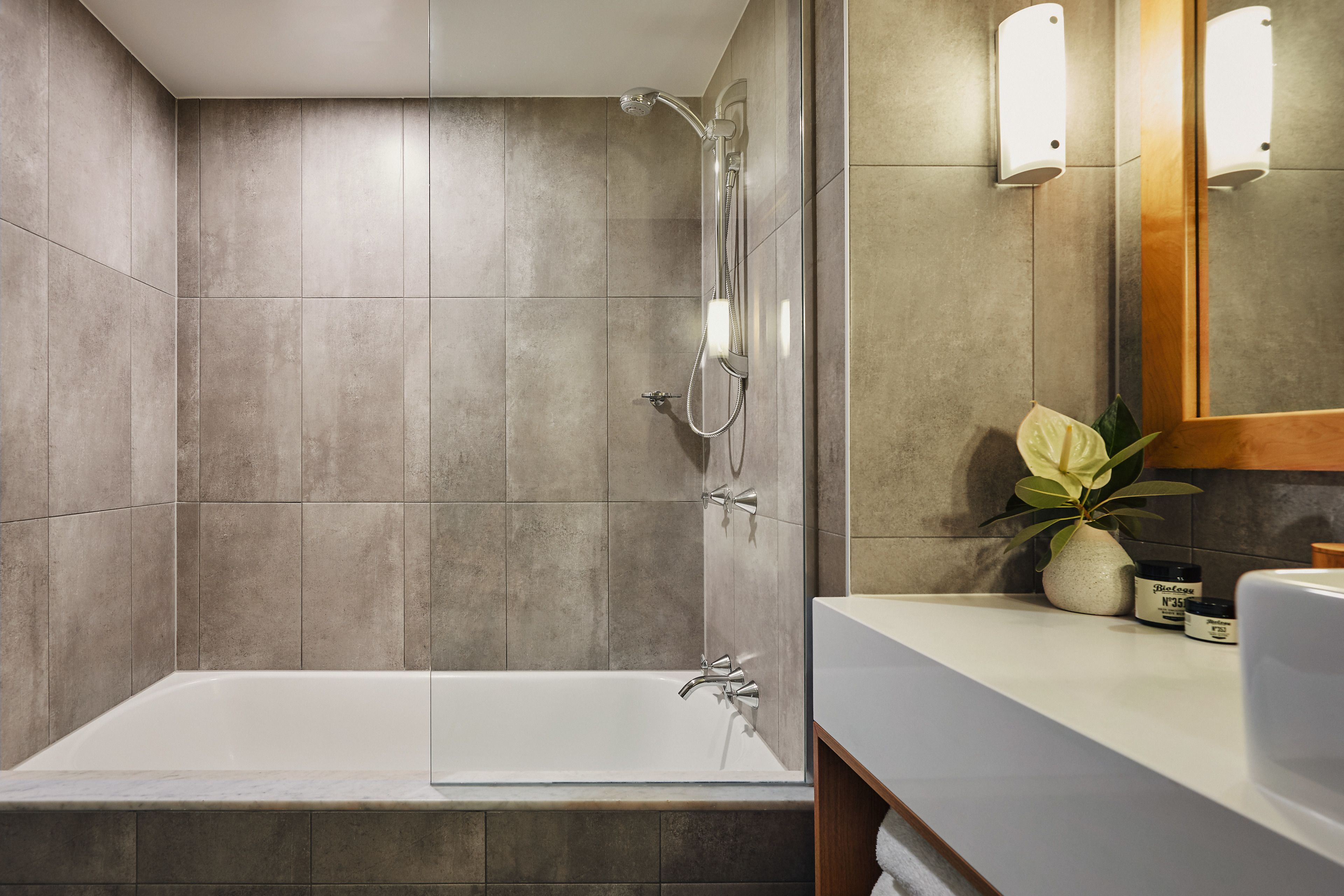 Ein modernes Badezimmer mit Badewanne, Dusche und Waschtisch mit Spiegel und Topfpflanze.