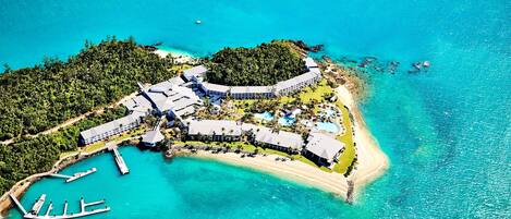 An aerial view of a resort with a beach, a marina, and lush greenery.