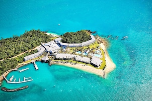 An aerial view of a resort with a beach, a marina, and lush greenery.